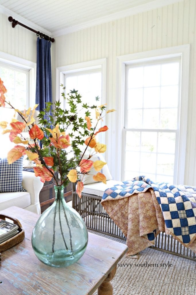 Clear light blue vase with autumn leaves in it on a side table.