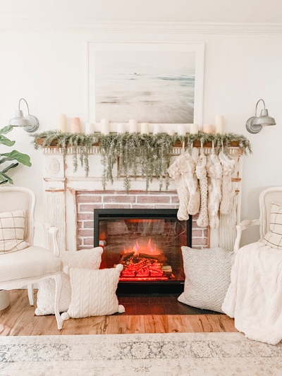 A cozy fireplace that is on with white pillows and stockings.