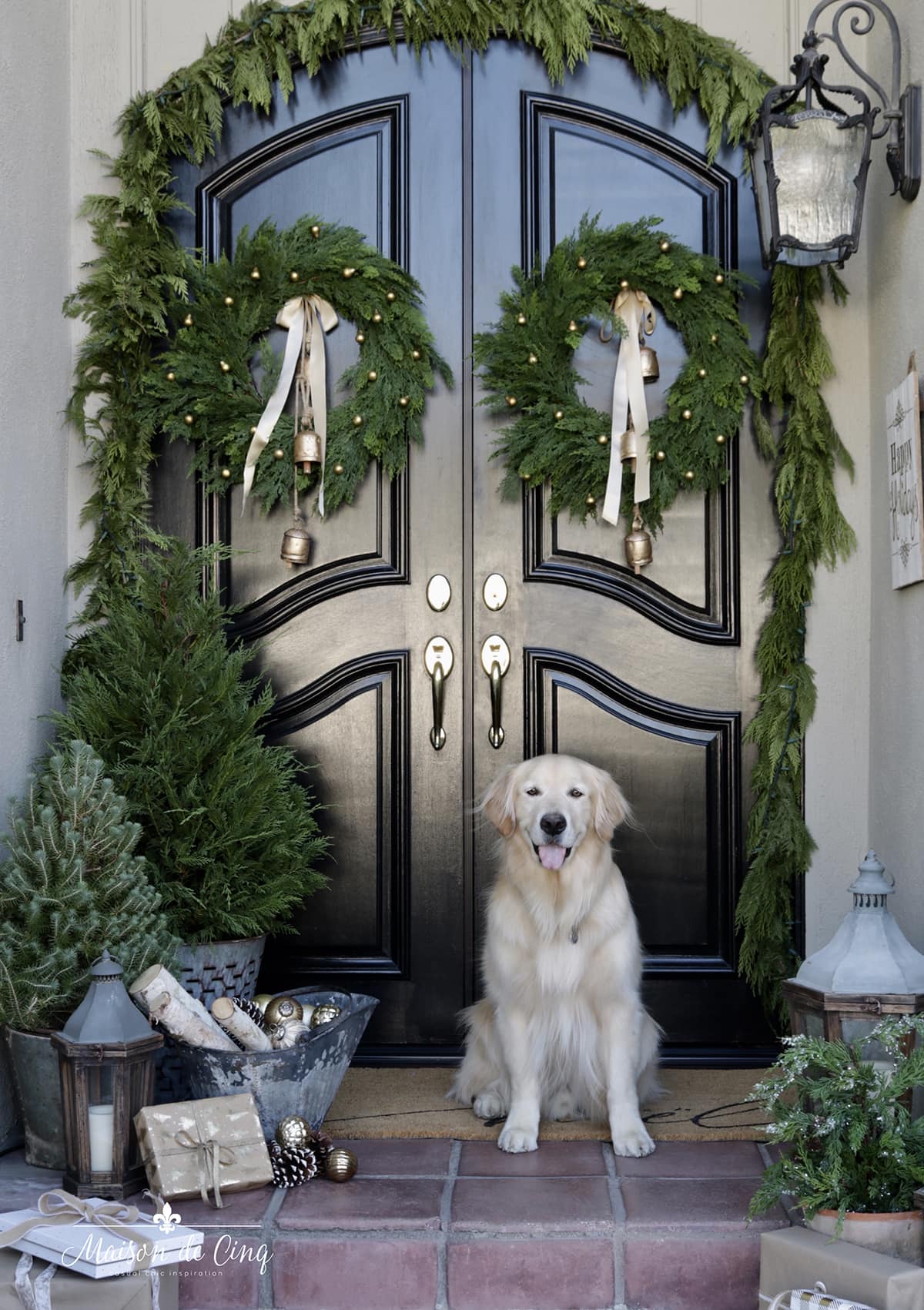traditional Christmas porch with greenery wreaths and golden retriever in front of black front doors 