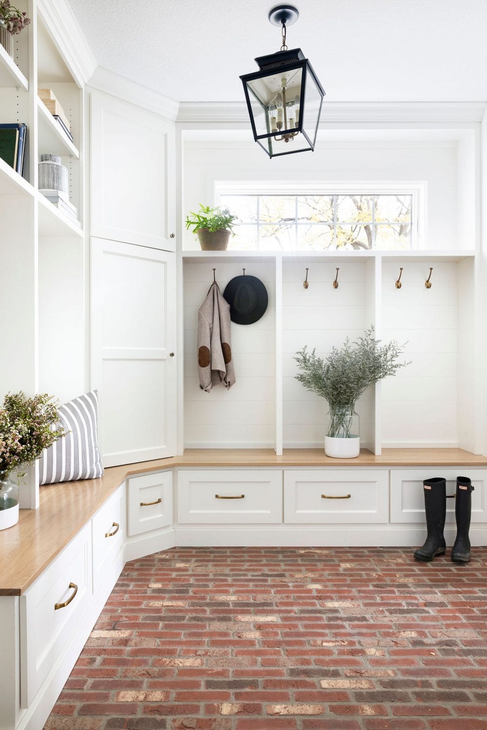 farmhouse style mudroom with white cabinets brick floors and vintage lantern