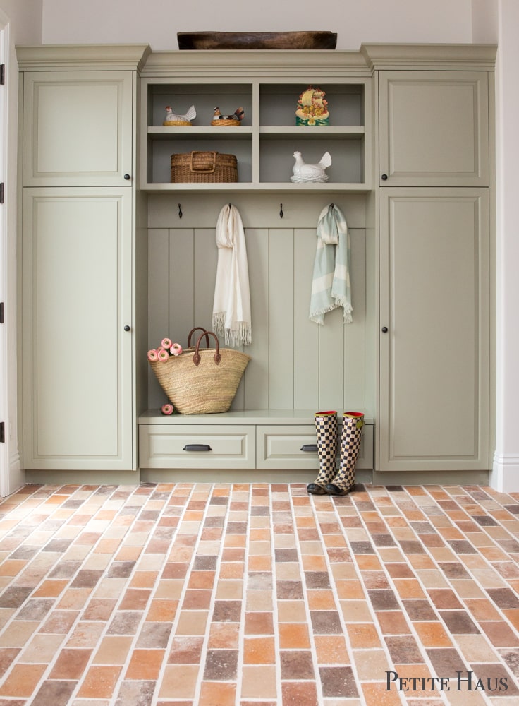 French inspired mudroom with pale green cabinets and brick floors 