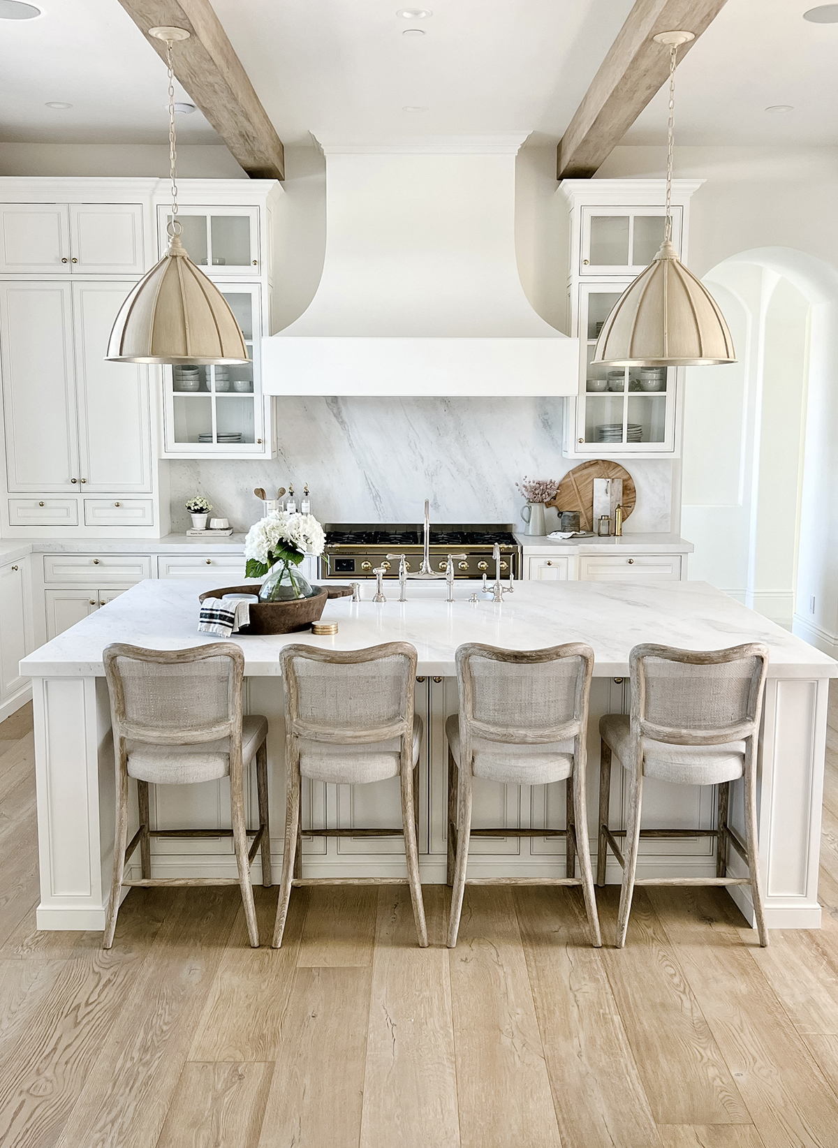 French country farmhouse white kitchen with stone range hood and wood beams 